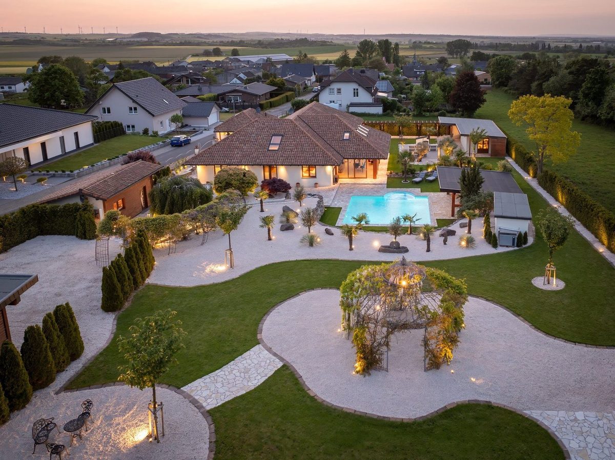 Villa mit beleuchtetem Garten aus der Luft bei Dämmerung